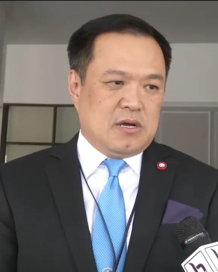 A man in a dark suit and blue tie speaking into microphones