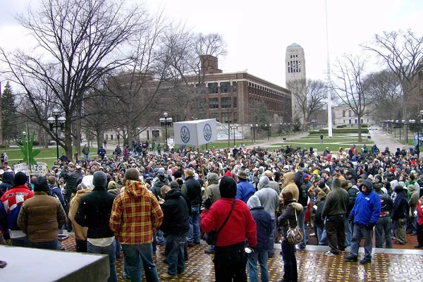 A crowd on a university square around a speaker and a large model of a cannabis leaf on a pole