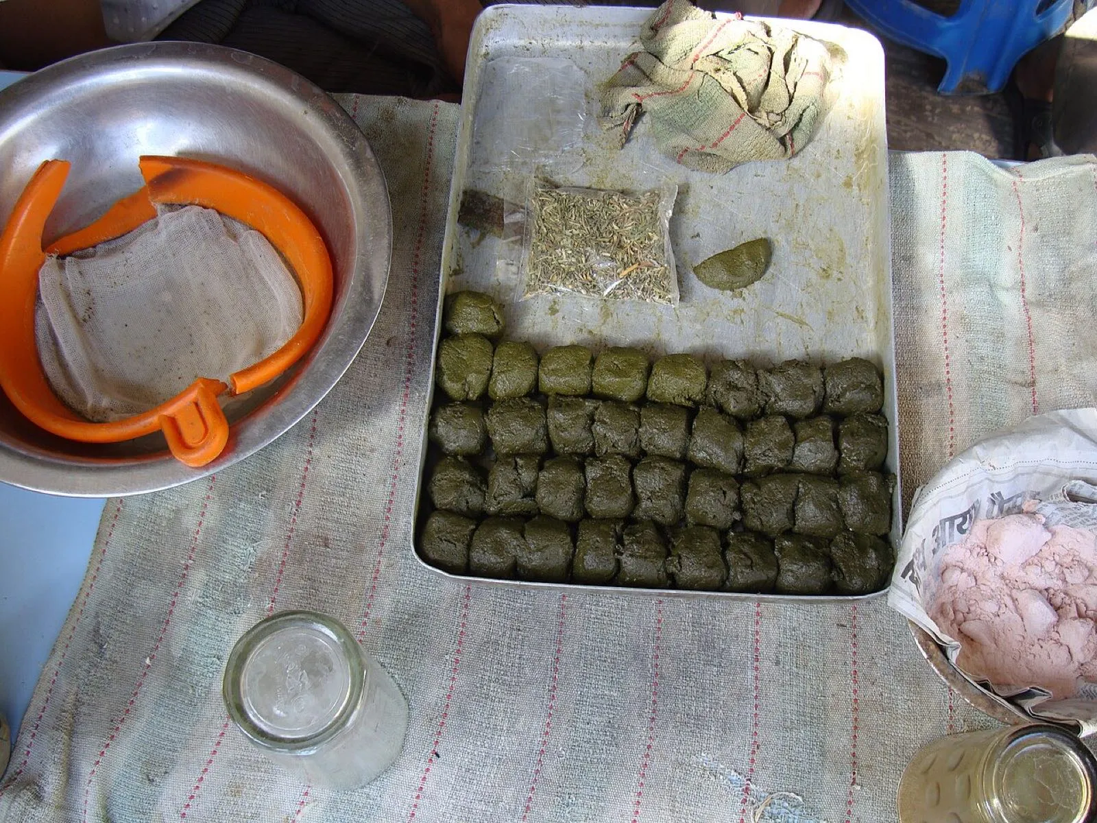 Balls of green bhang paste in a tray beside a bag of dried leaves