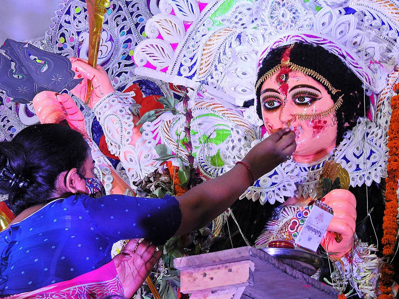 A woman in a blue sari touches sweets to the lips of a decorated image of the goddess Durga