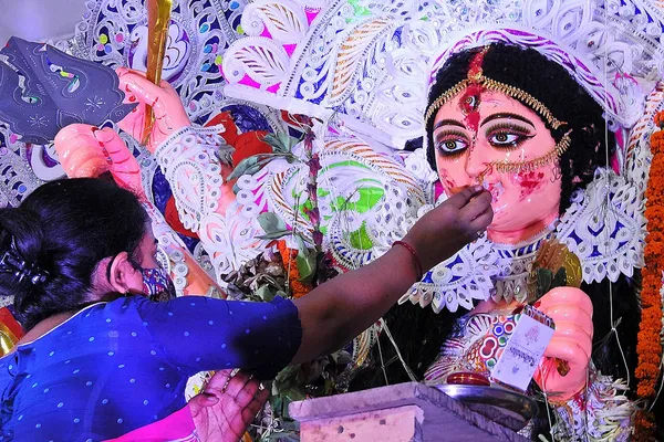A woman in a blue sari touches sweets to the lips of a decorated image of the goddess Durga