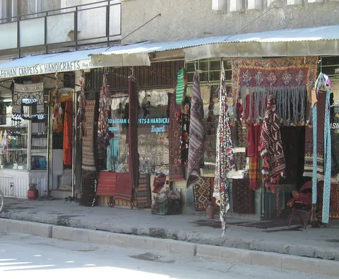 Carpet and handicraft shops with woven rugs hanging outside on Chicken Street in Kabul.