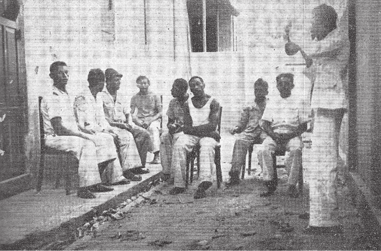 Historical black-and-white photograph of a group gathered in a Brazilian courtyard, with seated participants and one person standing at the right, reproduced as a clube de diambistas in Propriá, Sergipe.