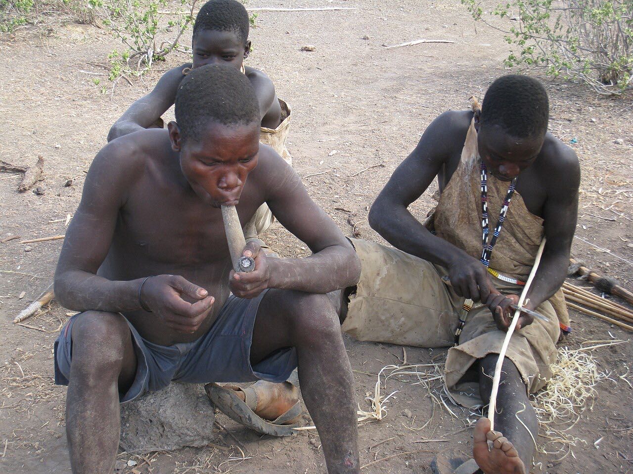 Hadza men sitting together, one of them smoking a pipe