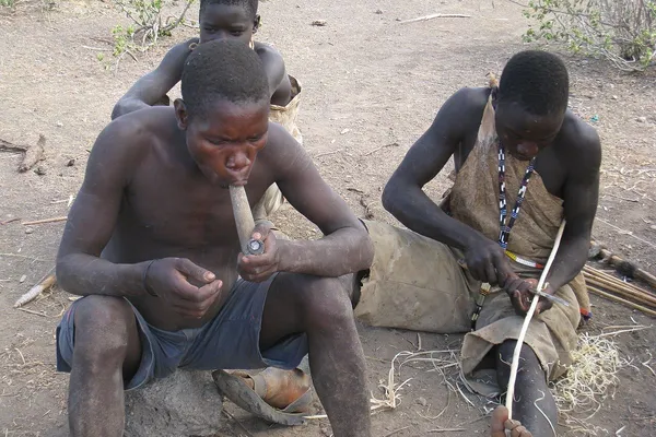 Hadza men sitting together, one of them smoking a pipe