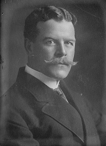 Black-and-white studio portrait of a man with a large moustache in a dark suit and tie