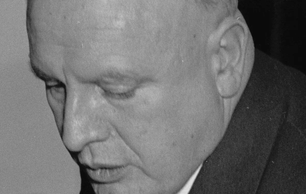 Black-and-white photograph of a heavy-set man in a suit looking down at papers
