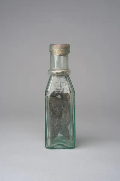 A sealed glass bottle holding dark lumps of cannabis resin