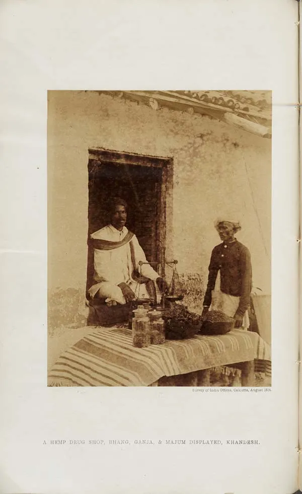 A vendor sitting in a doorway behind a table with jars and baskets of hemp drugs, a second man standing beside it.