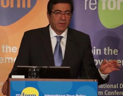 A man in a dark suit and tie speaking at a lectern in front of conference banners