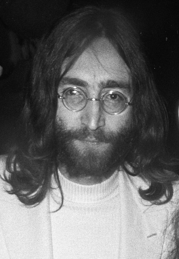 Black-and-white portrait of John Lennon with long hair, a beard and round glasses.