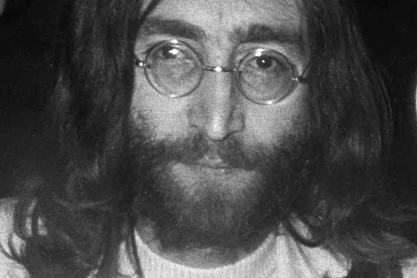 Black-and-white portrait of John Lennon with long hair, a beard and round glasses.