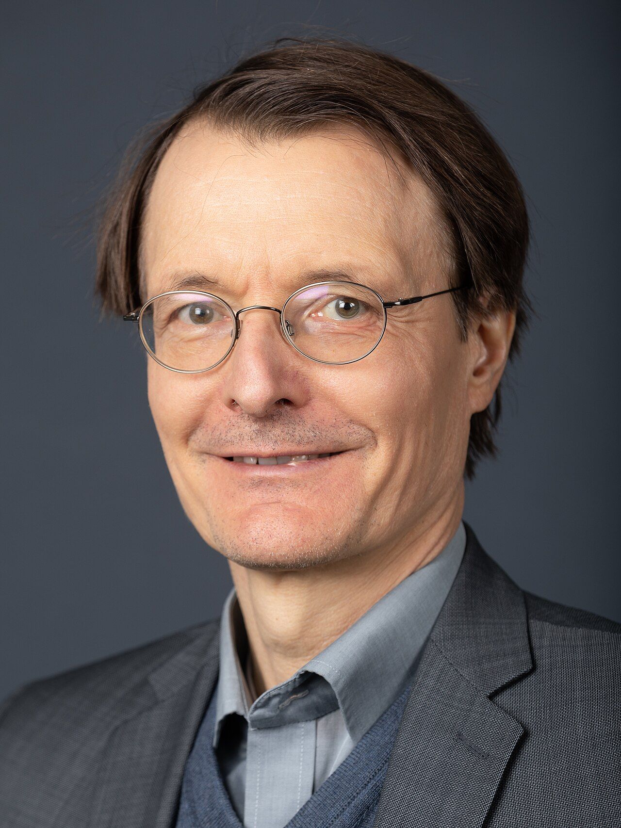 Portrait of a man with grey hair and glasses in a dark jacket