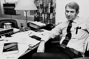 Black-and-white photograph of Lester Grinspoon wearing a tie and seated beside a desk in an office.