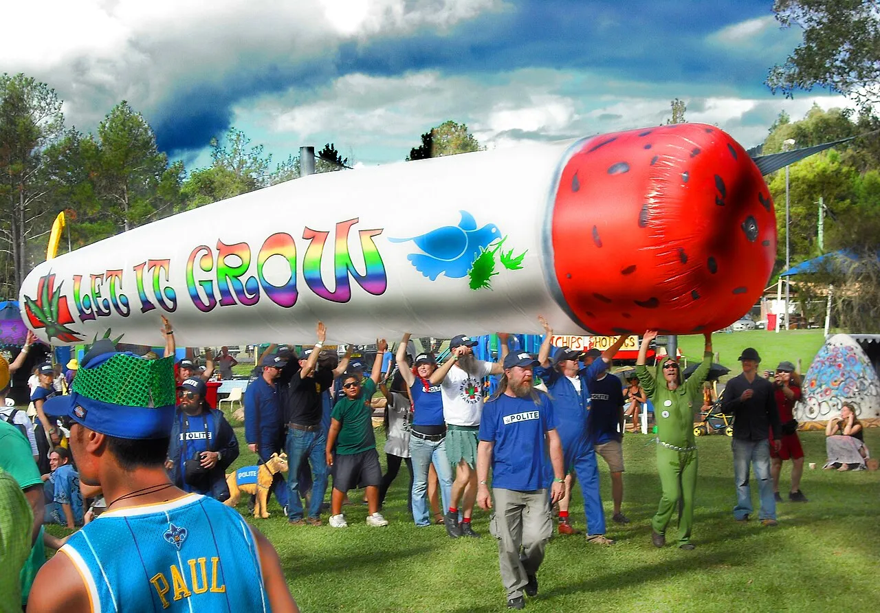 A crowd carrying a giant inflatable joint across a park