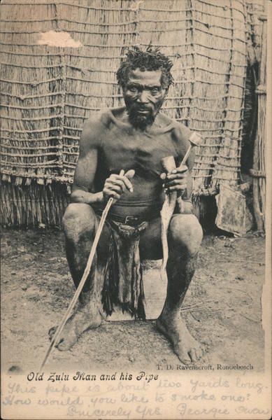 Vintage South African postcard depicting an older Zulu man seated outside a traditional dwelling holding a long smoking pipe.