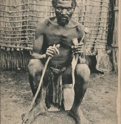 Vintage South African postcard depicting an older Zulu man seated outside a traditional dwelling holding a long smoking pipe.