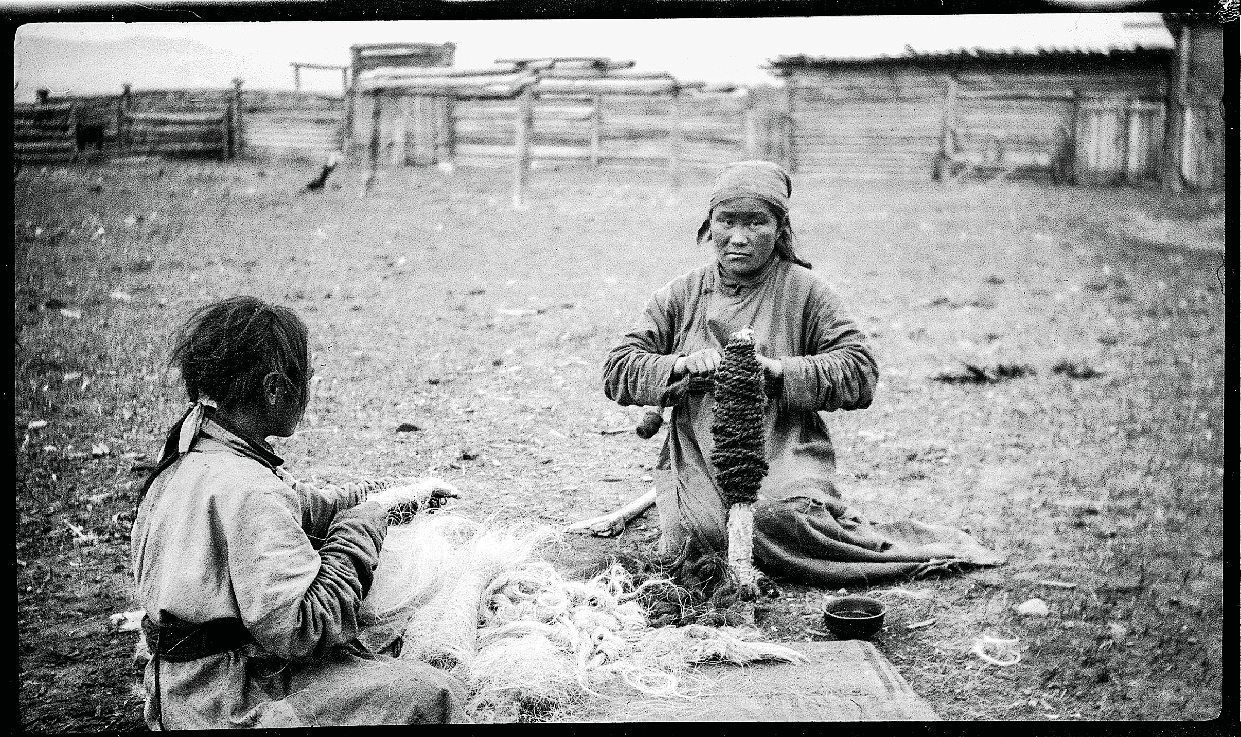 Historical black-and-white photograph showing two Mongolian women preparing and coiling rope outdoors in 1928.