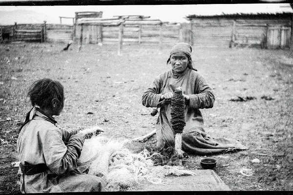 Historical black-and-white photograph showing two Mongolian women preparing and coiling rope outdoors in 1928.