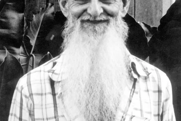 Black-and-white photograph of an elderly man with a long white beard, smiling, in a checked shirt
