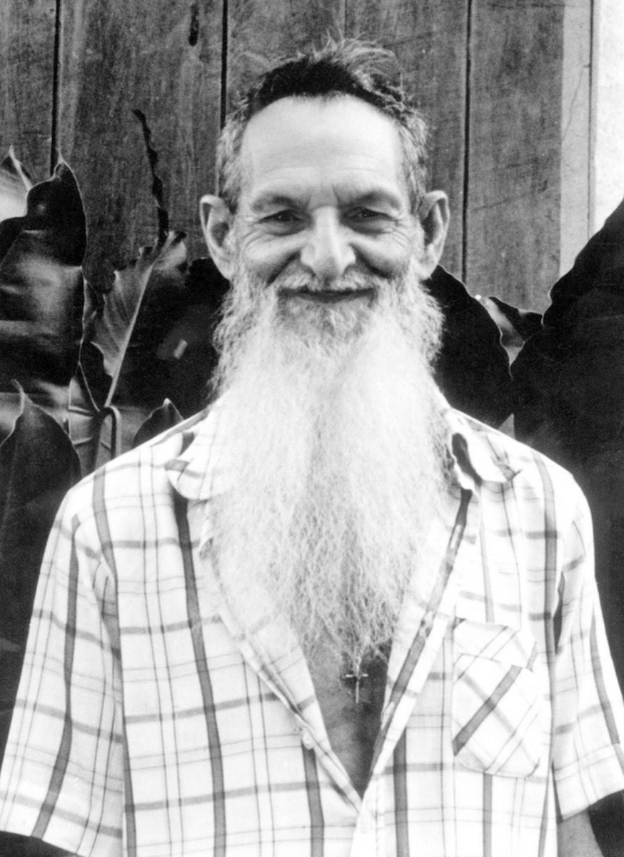 Black-and-white photograph of an elderly man with a long white beard, smiling, in a checked shirt