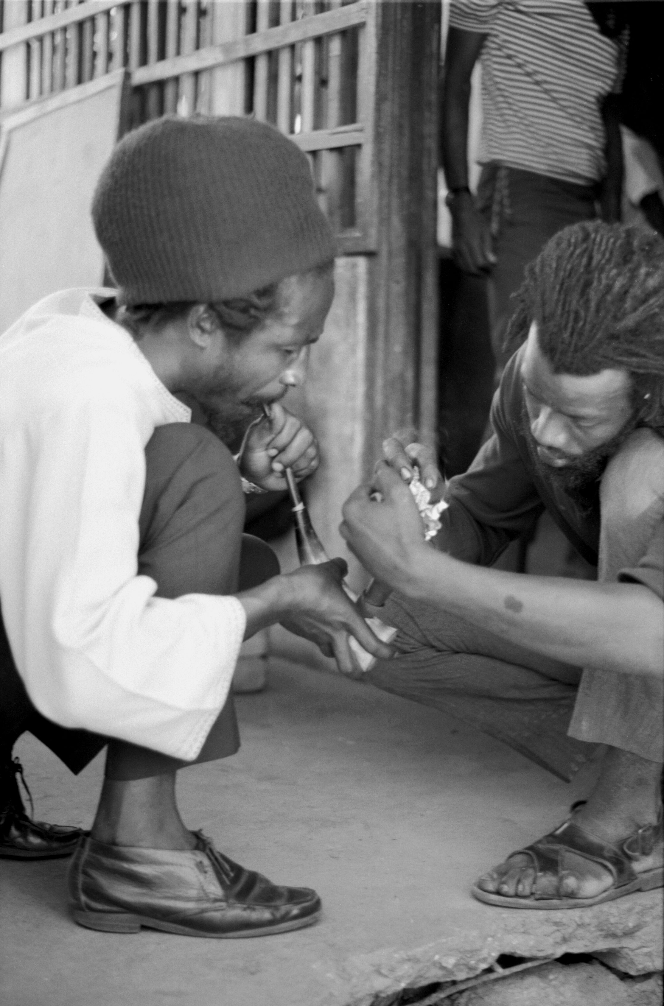 Historical photograph of two Rastafari participants lighting and smoking a communal cannabis chalice during a religious ceremony in Kingston.