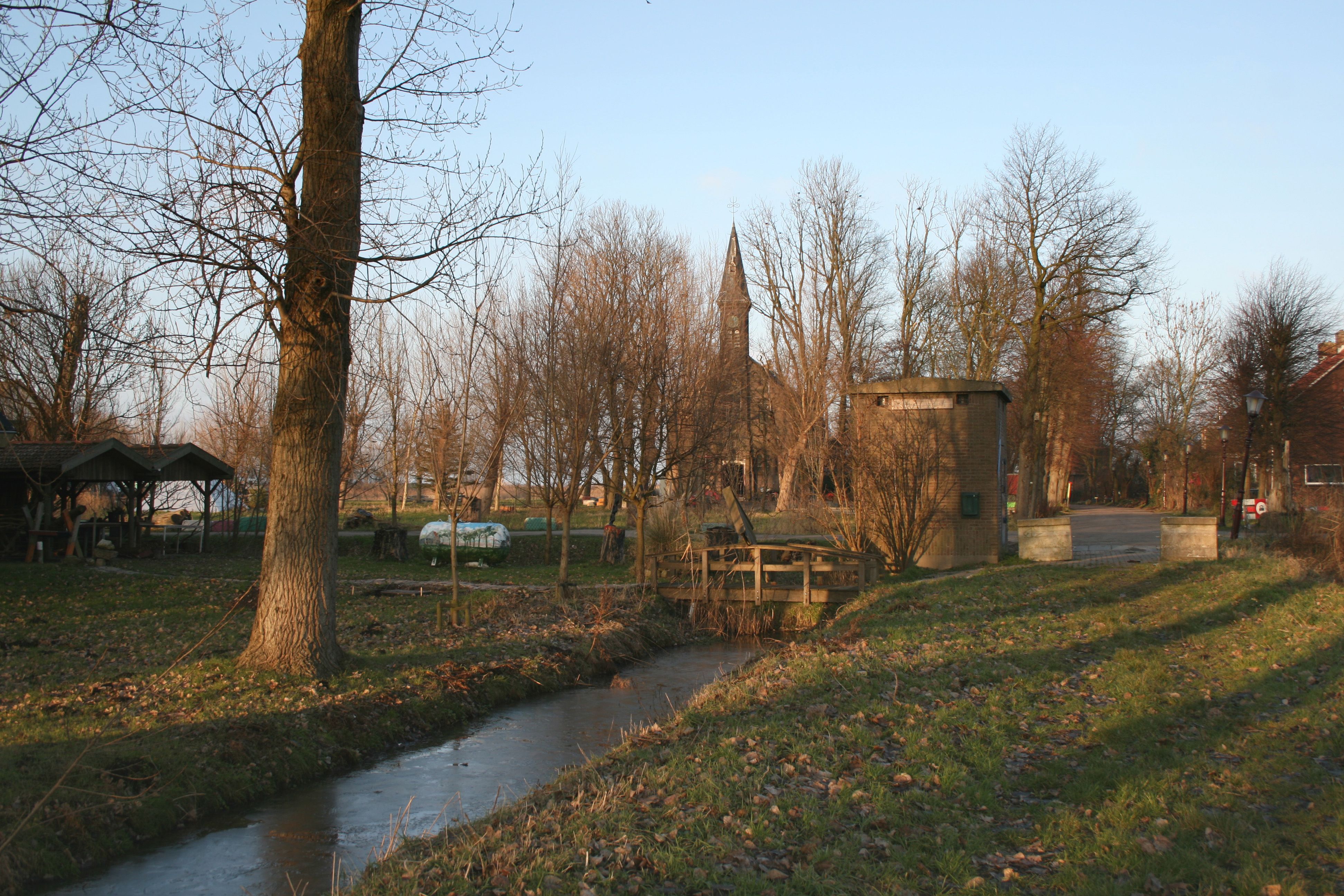 A frozen ditch and trees beside the old church and village buildings at Ruigoord.