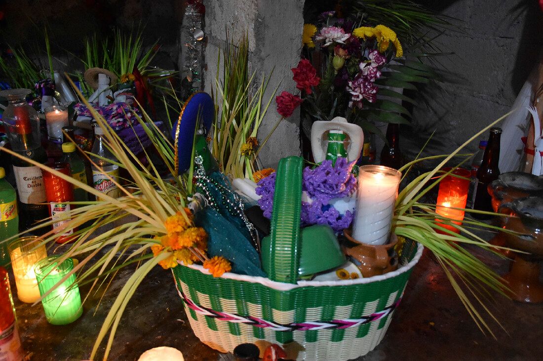 Traditional Otomí ceremonial basket decorated with flowers and greenery, surrounded by candles, drinks, and sacred offerings.