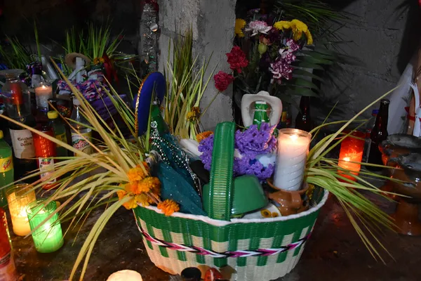 Traditional Otomí ceremonial basket decorated with flowers and greenery, surrounded by candles, drinks, and sacred offerings.
