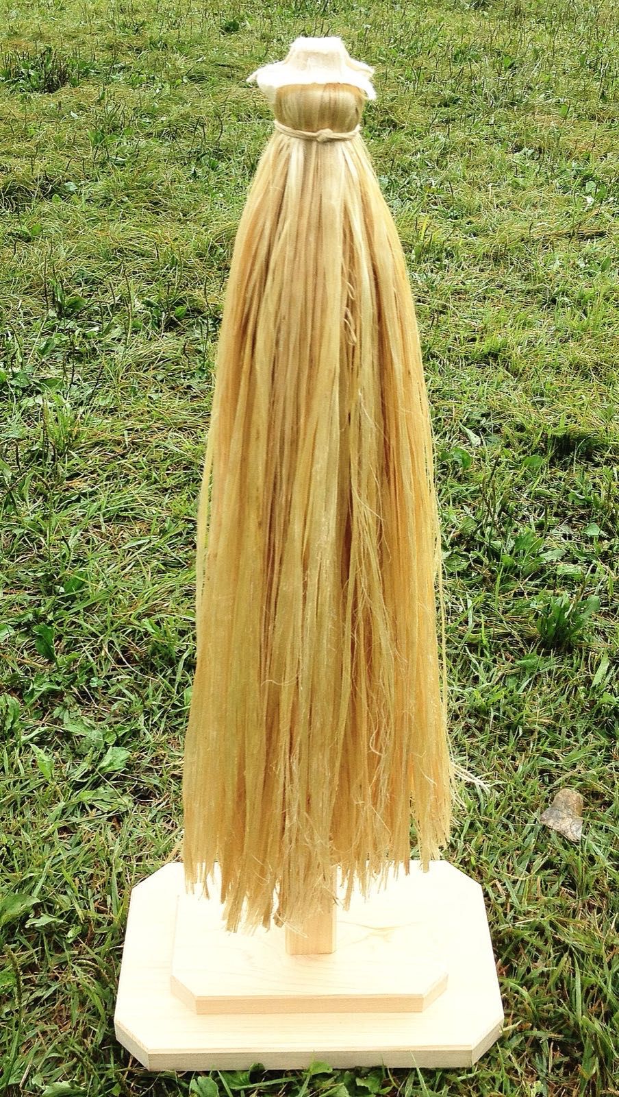 A wooden wand hung with long strands of pale hemp fibre