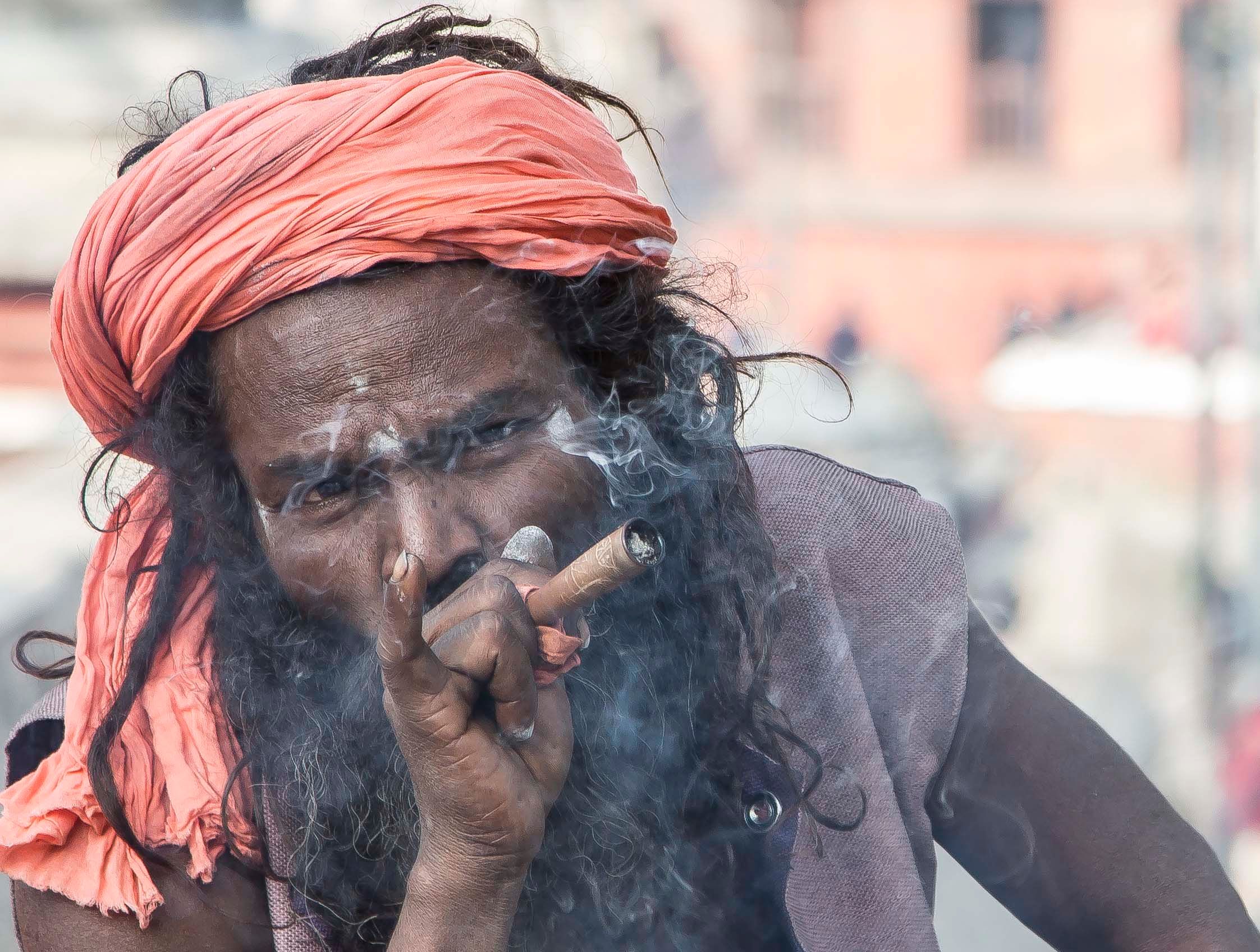 A sadhu wearing a red head wrap smokes a cannabis cigarette at Pashupatinath in Nepal