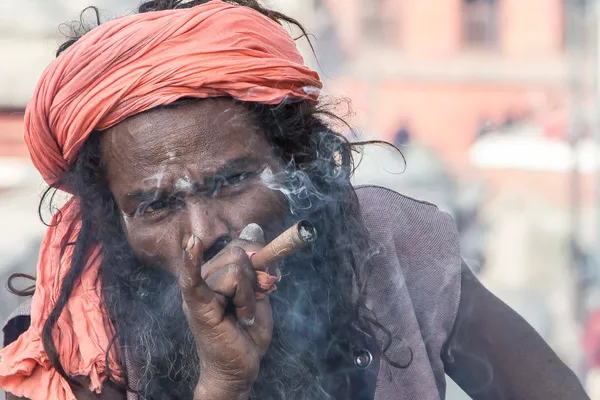 A sadhu wearing a red head wrap smokes a cannabis cigarette at Pashupatinath in Nepal