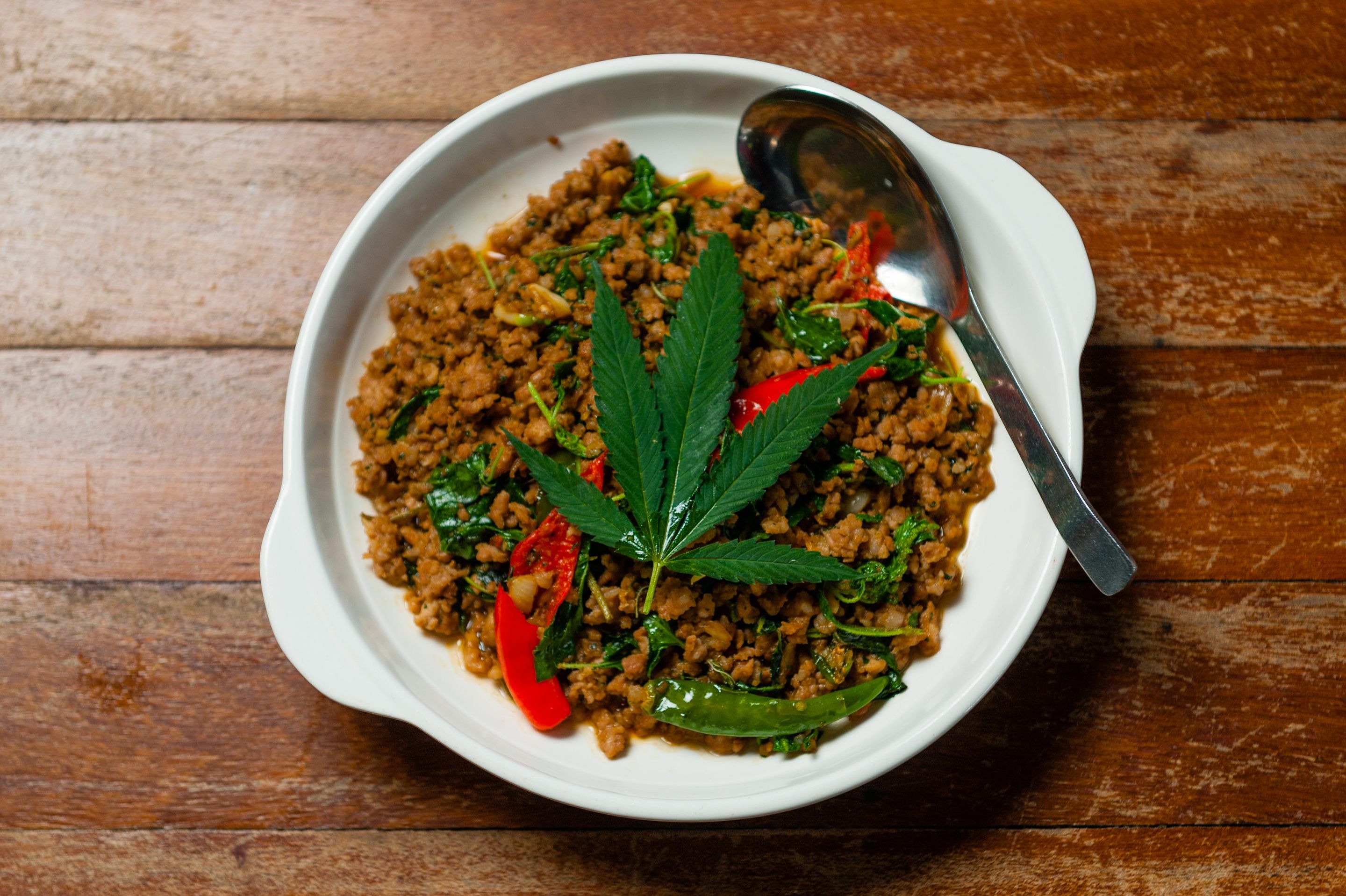 Thai minced pork and basil stir-fry served in a white bowl, garnished with a fresh cannabis leaf.