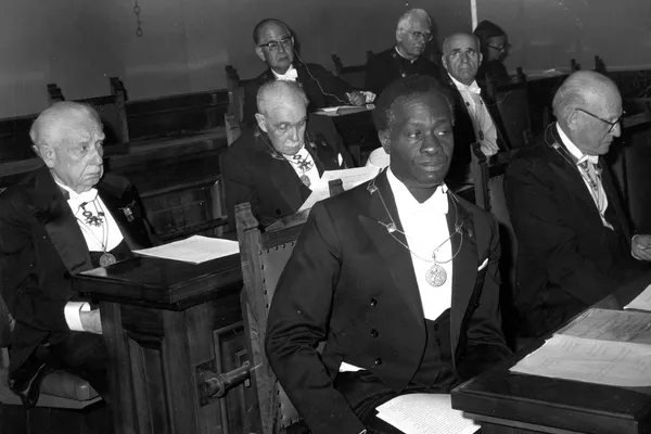 Historical black-and-white photograph of Nigerian psychiatrist Thomas Adeoye Lambo seated at an academic gathering in 1975, wearing a ceremonial medallion.
