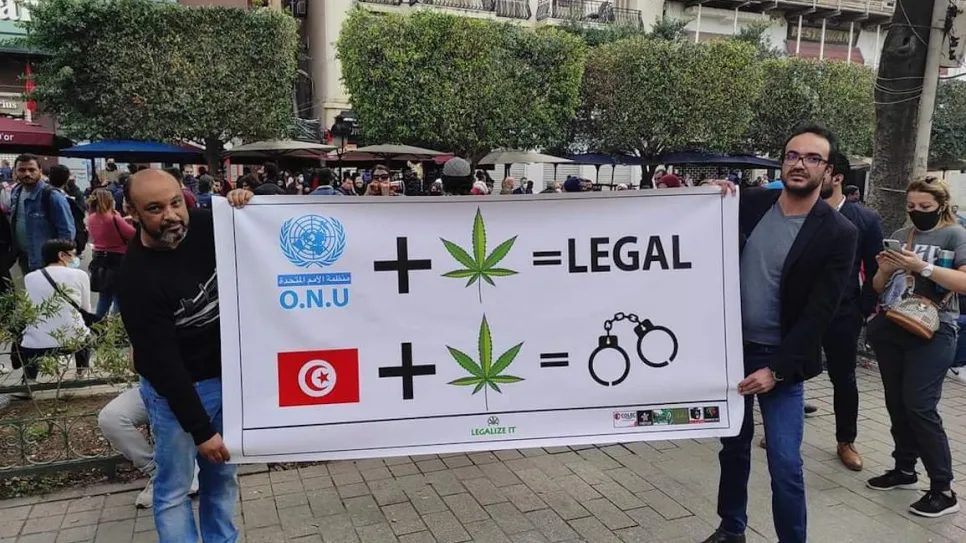 Tunisian cannabis legalization activists holding a banner featuring cannabis leaves and handcuffs to criticize punitive drug laws.